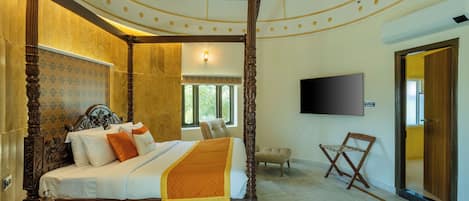 A four-poster bed with a wooden frame and white bedding, a flat-screen TV mounted on the wall, and a small wooden chair.