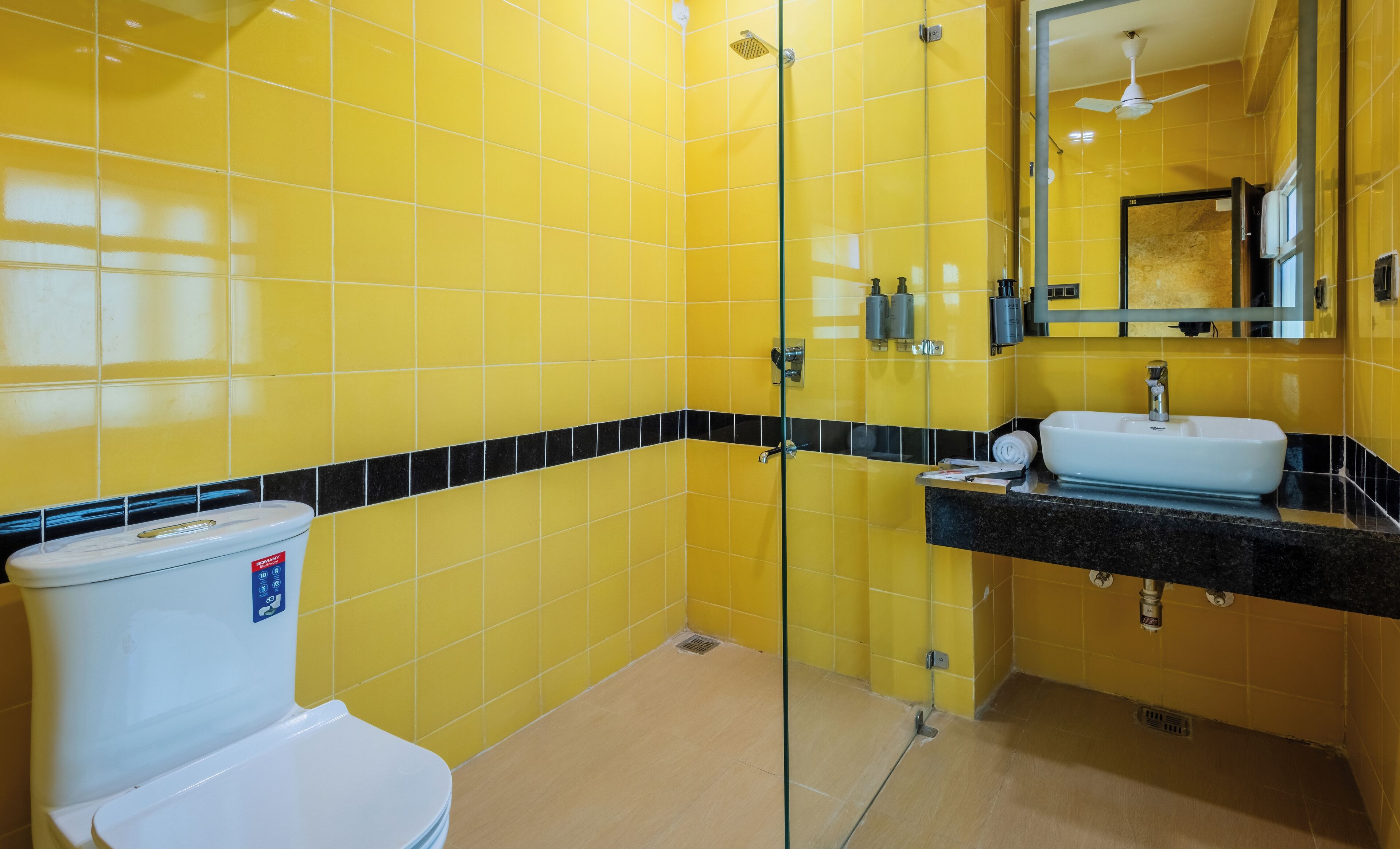 A bathroom with yellow tiled walls, a glass shower enclosure, a white toilet, and a sink with a black countertop.
