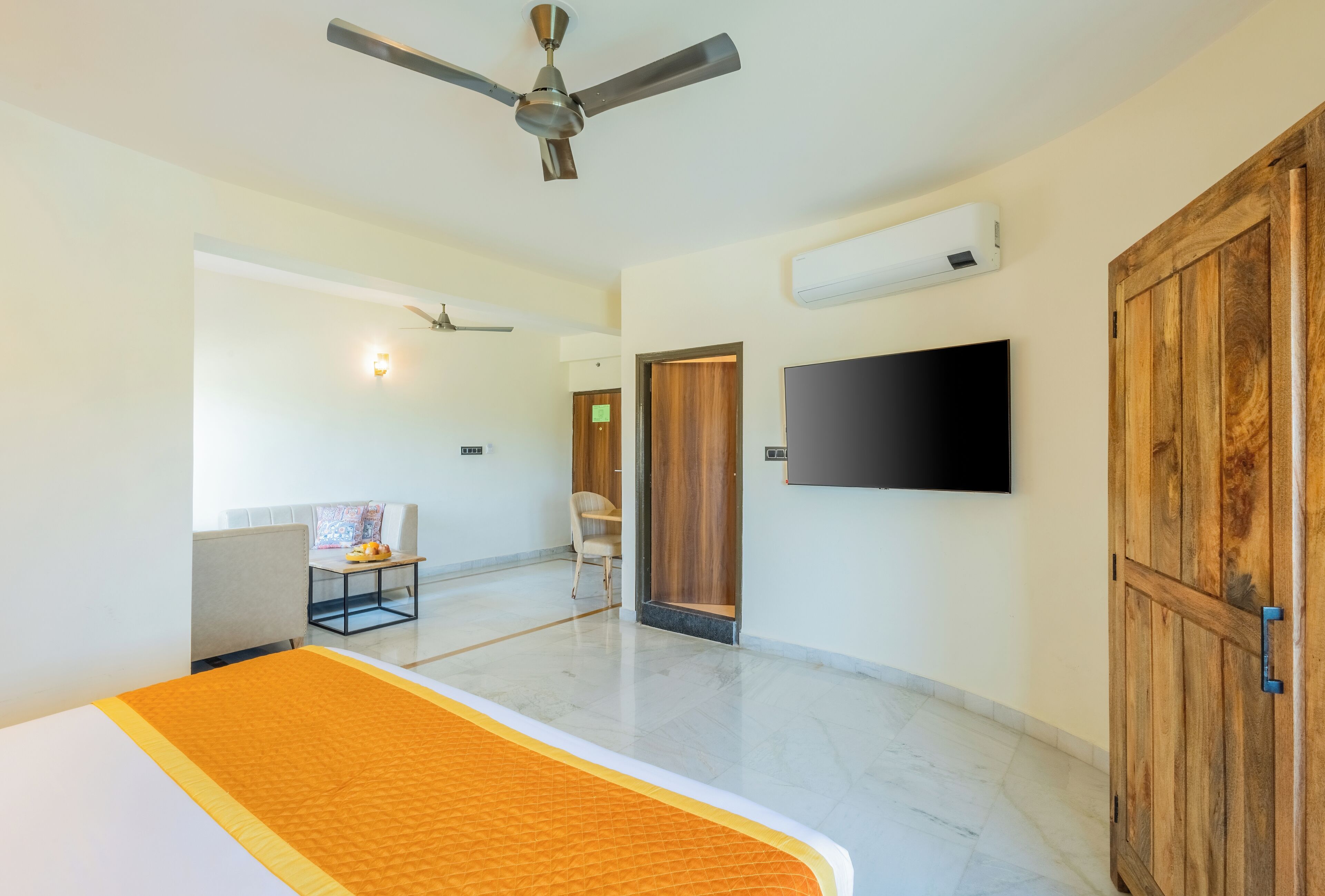 A hotel room with a bed, a ceiling fan, a TV, a wardrobe, and a small table with a chair.