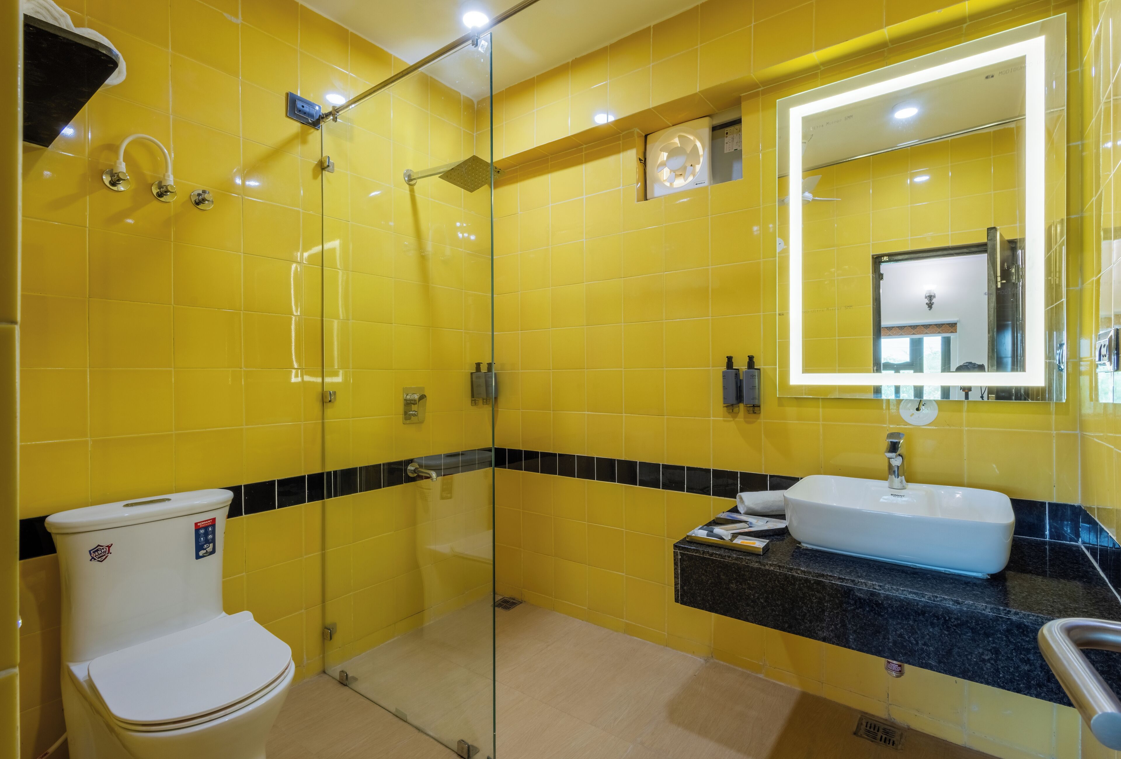 A bathroom with yellow tiles, a glass-enclosed shower, a white toilet, and a sink with a mirror above it.