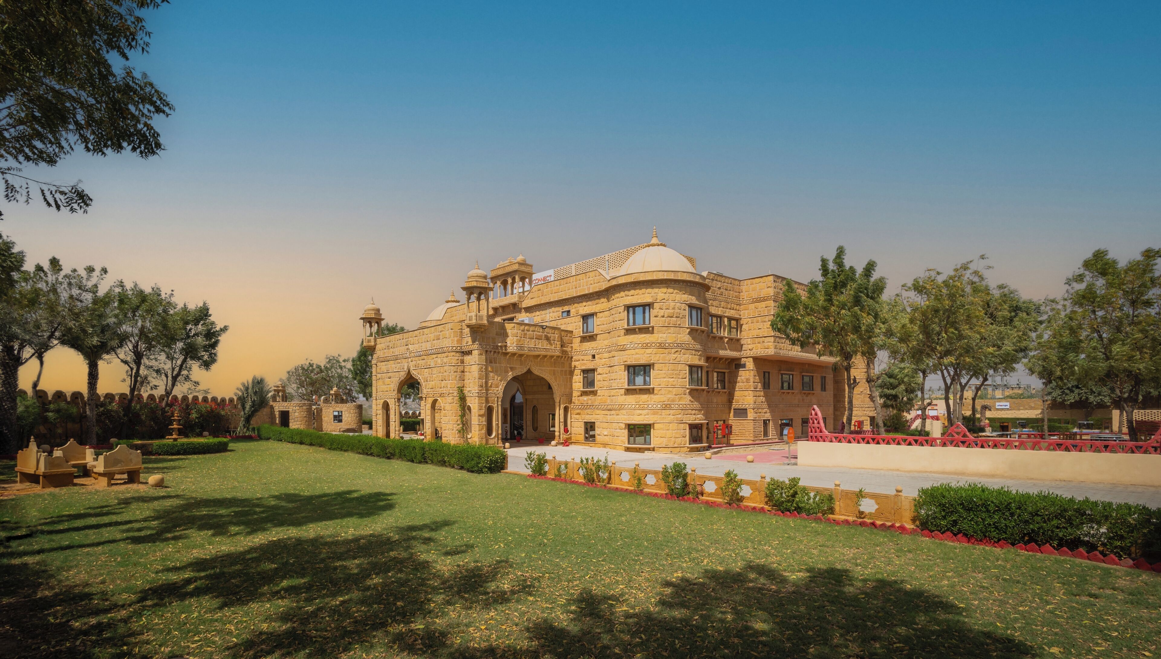 A historic building with a large central archway, surrounded by a well-maintained lawn and trees.