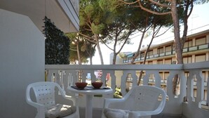 A balcony with two white plastic chairs, a small round table, and a bowl. - Chic holiday apartment with shared pool (Lignano Sabbiadoro)