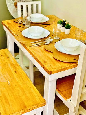A dining area with a table set for two, featuring a chair and bench, white plates, glassware, and cutlery.