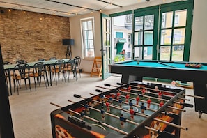 A room with a pool table, chairs, and a foosball table.