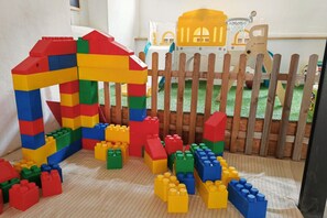 A play area with a wooden fence, a small playhouse, and scattered building blocks.