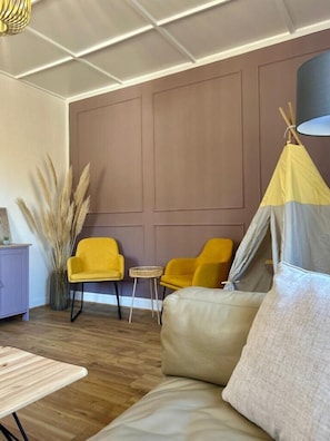 A room with a sofa, two yellow chairs, a small table, a lamp, and a tent-like structure.