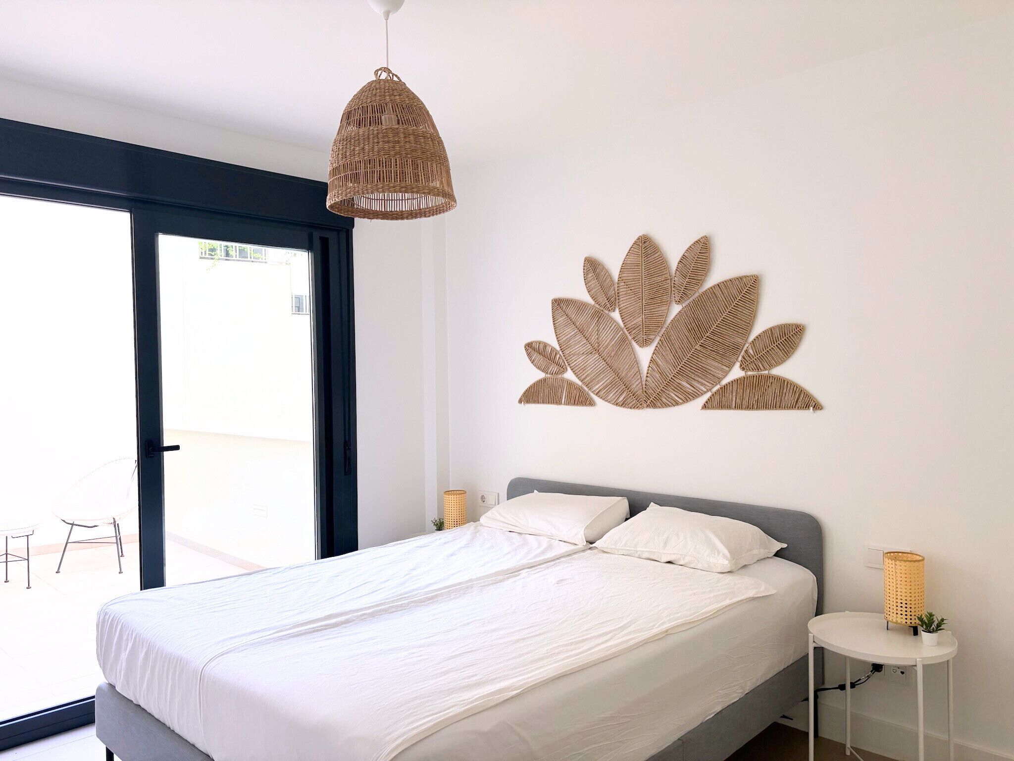 A bedroom with a bed, a hanging light fixture, a wall art piece, and a small table with a plant.