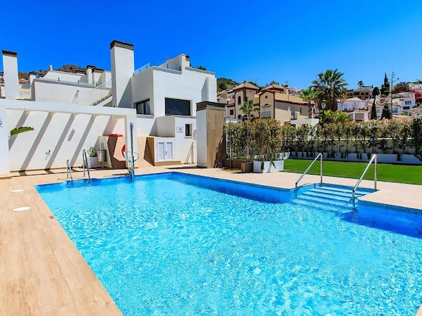A swimming pool with a clear blue water, surrounded by a white building with a modern design, and a well-maintained lawn area.