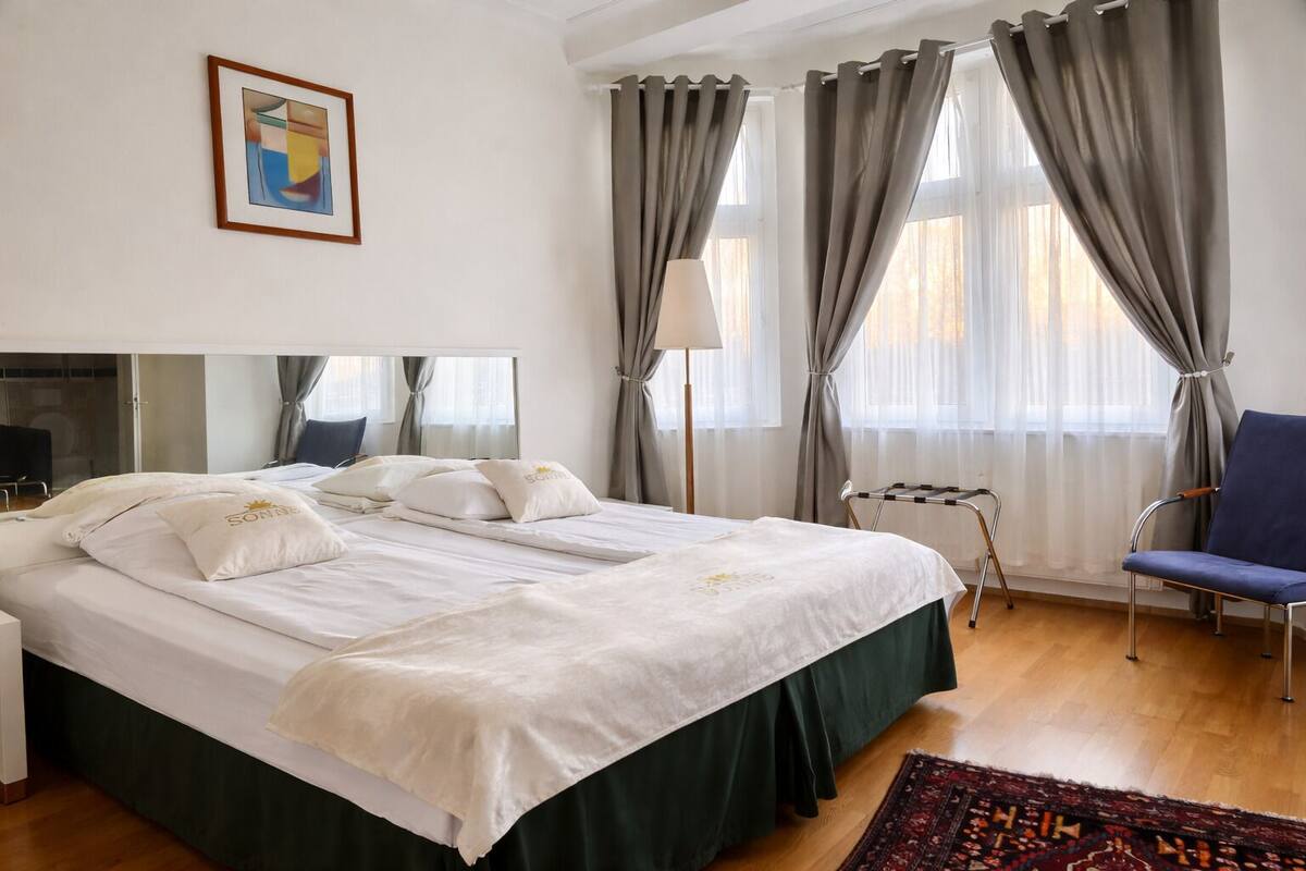 A hotel room with a large bed, a chair, a desk, and a window with curtains.