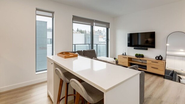 Una cucina moderna con isola centrale, sgabelli da bar, un armadietto in legno, una TV a parete e ampie finestre.