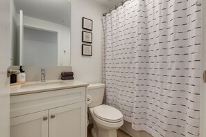 Ein Badezimmer mit einem weißen Waschbecken, Spiegel und Toilette. An der Wand hängen drei Bilder in Rahmen.