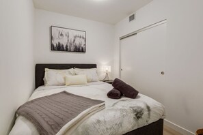 Ein Schlafzimmer mit einem Bett, Kissen, einer Decke, einem gefalteten Handtuch, einer Nachttischlampe und einem gerahmten Bild an der Wand.