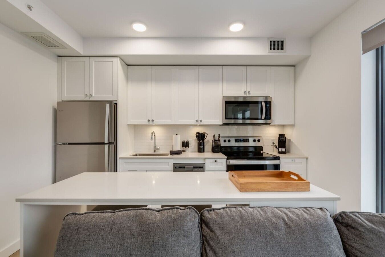 A modern kitchen with white cabinets, a stainless steel refrigerator, a microwave, and a stove.