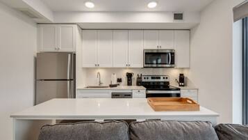A modern kitchen with white cabinets, a stainless steel refrigerator, a microwave, and a stove.