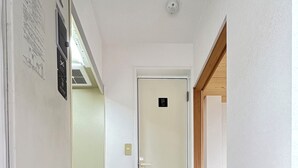 A hallway with a wooden floor, a blue mat at the entrance, and a door marked with a number. - Along the airport line, nearest stations Hanazonomachi and Haginochaya 2 min. each [ 305] Japanese-style room with mini-kitchen and private bathroom, excellent access [ 305]. (大阪市)