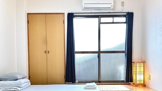 A hotel room with a wooden ceiling, a sliding glass door, a bed with white linens, and a traditional Japanese lantern. - Along the airport line, nearest stations Hanazonomachi and Haginochaya 2 min. each [ 305] Japanese-style room with mini-kitchen and private bathroom, excellent access [ 305]. (大阪市)