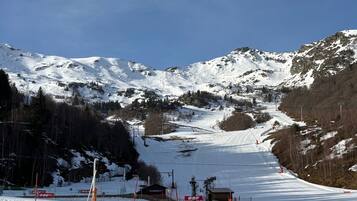 Une piste de ski avec un télésiège, des montagnes enneigées et un petit bâtiment avec des panneaux indicateurs.