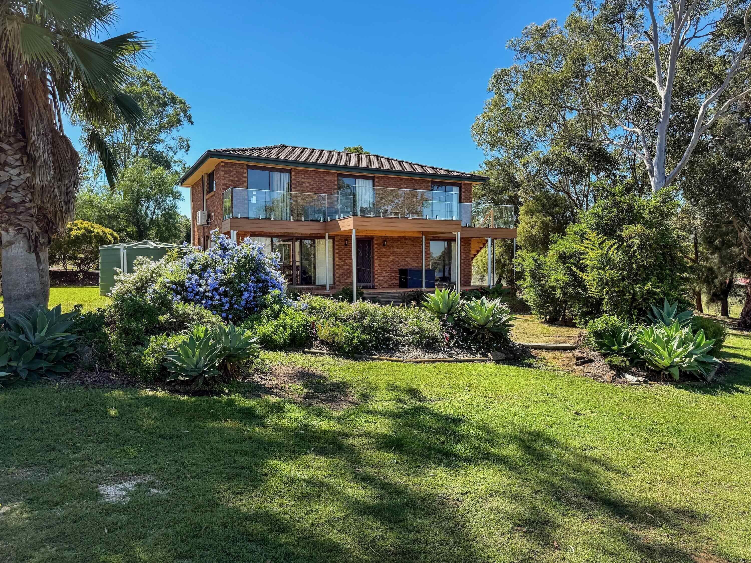 A two-story house with a balcony, surrounded by a well-maintained garden with various plants and trees.