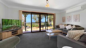 A living room with a TV, a sofa, a coffee table, and a sliding glass door leading to a garden. - Hunter Homestead - Affordable accommodation in a prime Lovedale location (LOVEDALE)
