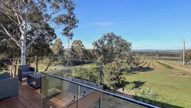 A deck with outdoor furniture, a glass railing, and a view of a grassy landscape with trees. - Hunter Homestead - Affordable accommodation in a prime Lovedale location (LOVEDALE)