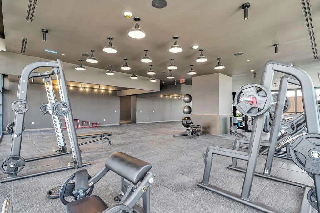 A gym with various exercise equipment, including weight machines and free weights, and a large mirror.