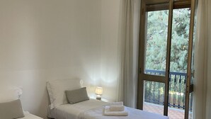 Une chambre d’hôtel avec un lit, une table de chevet, une lampe et une vue sur un balcon bordé d’arbres.