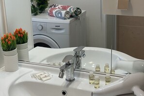 Kylpyhuoneessa on valkoinen pesuallas, peili ja pyykinpesukone, joka näkyy taustalla.