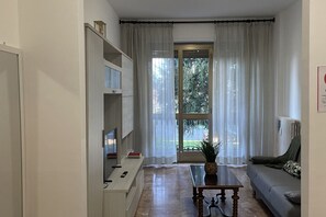 Ett modernt vardagsrum med en tv, ett soffbord och en soffa. Det finns ett stort fönster med gardiner och en växt på bordet.