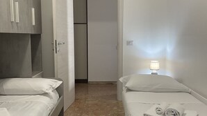 Une chambre d’hôtel avec deux lits, une armoire, une porte et une table de chevet avec une lampe.