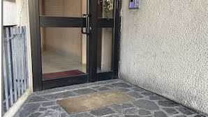 Un hall d’entrée au sol en pierre, avec une porte, un paillasson et un mur à texture.