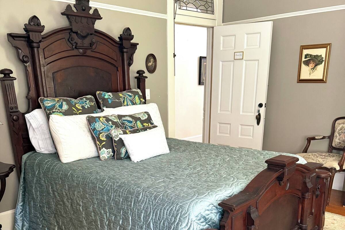 Un dormitorio con una cama de madera, un edredón estampado, una alfombra y una puerta.