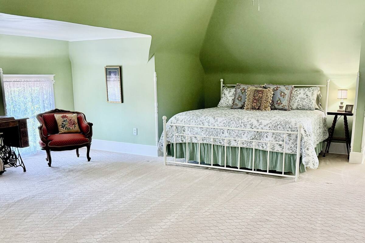Un dormitorio con una cama grande, una silla, una mesita y una ventana con cortinas.