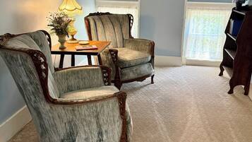 A room with two upholstered chairs, a table with a lamp, and a bookshelf.