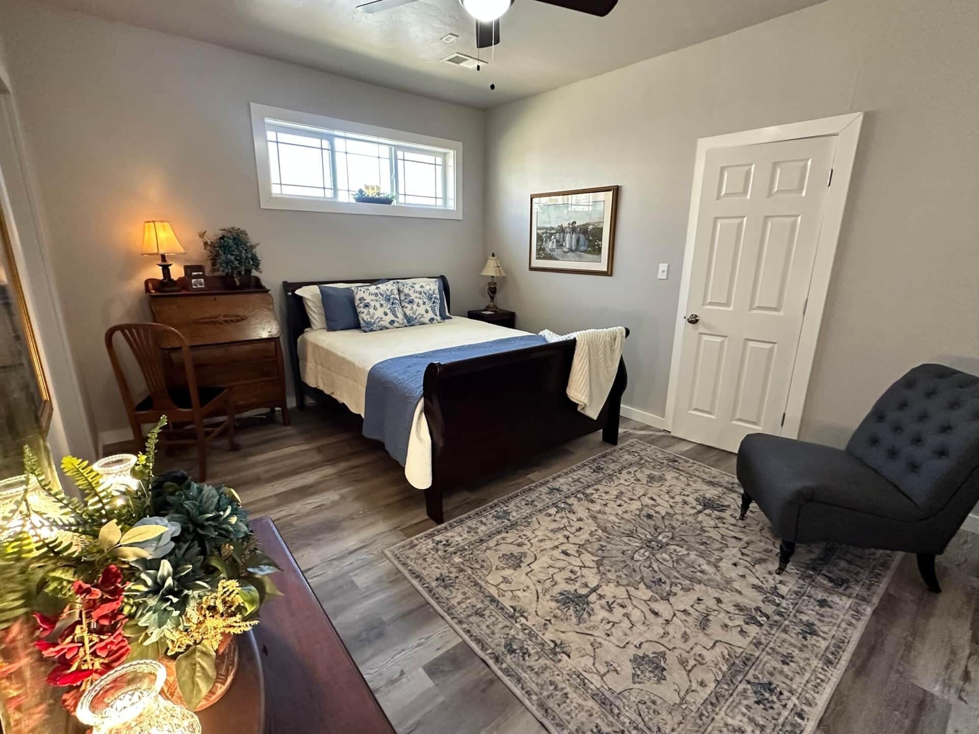 A bedroom with a bed, a desk, a chair, a door, and a window.
