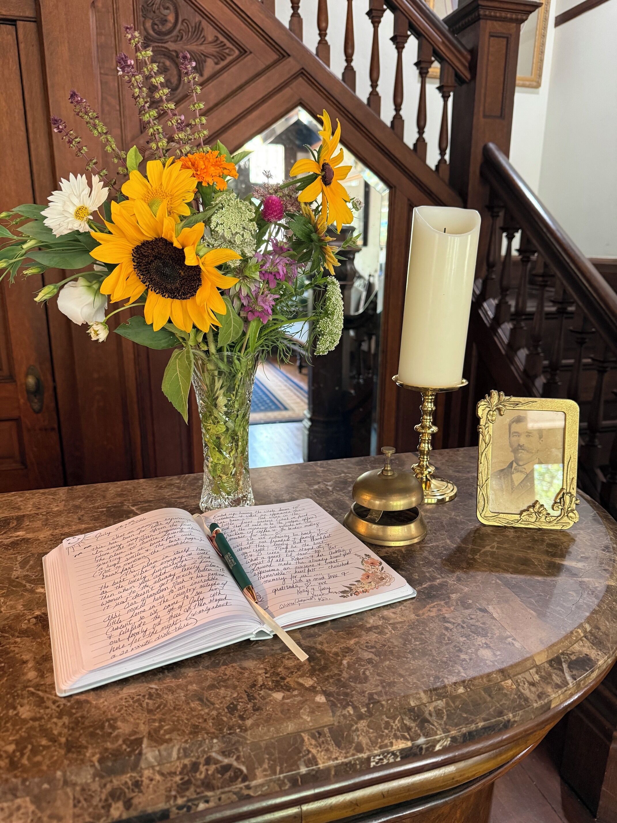 A marble table with a notebook, a pen, a candle, a decorative frame, and a vase with flowers.