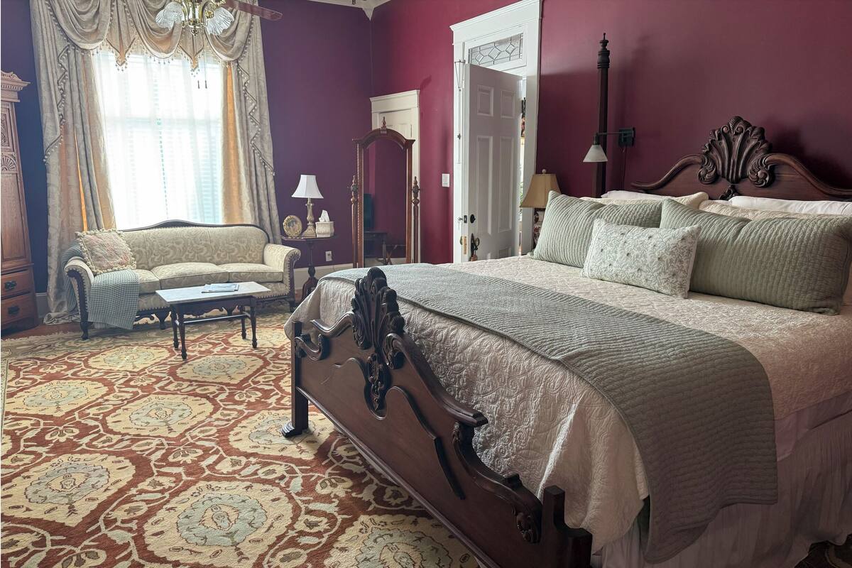 Un dormitorio con una cama grande, un sofá, piso de madera y alfombra estampada.
