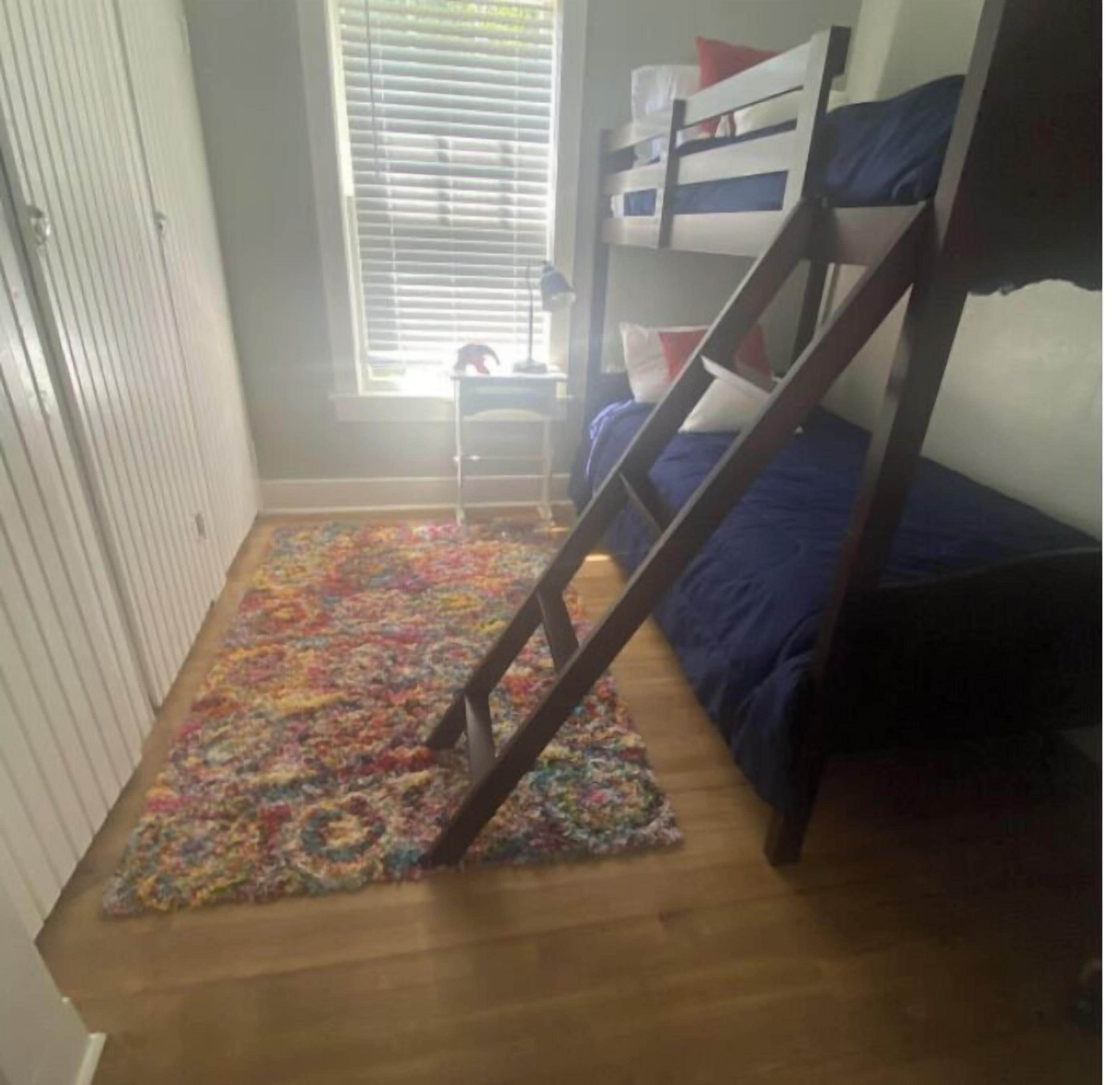 A room with a bunk bed, a small desk, and a colorful rug.
