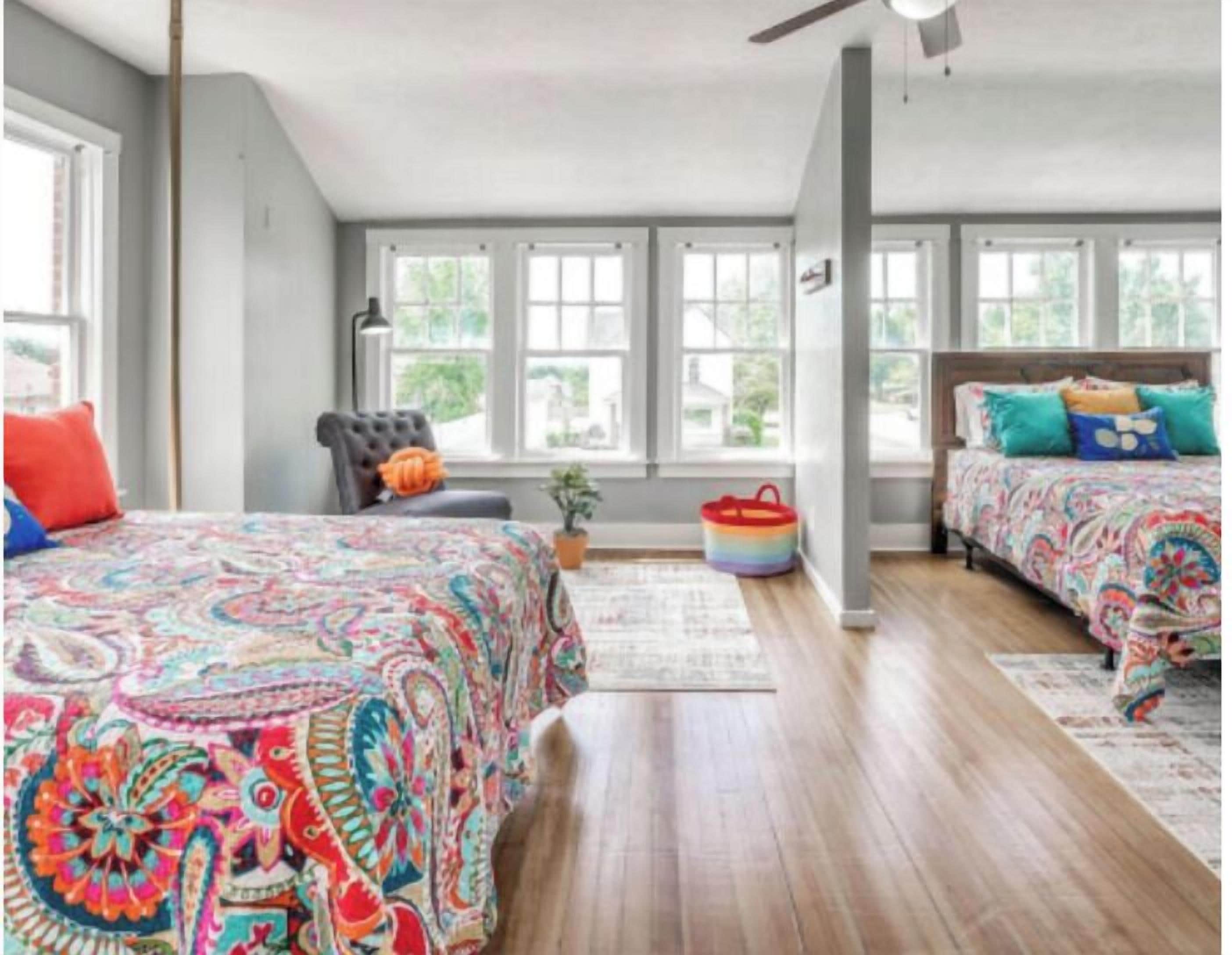 A bedroom with two beds, a chair, a ceiling fan, and large windows.