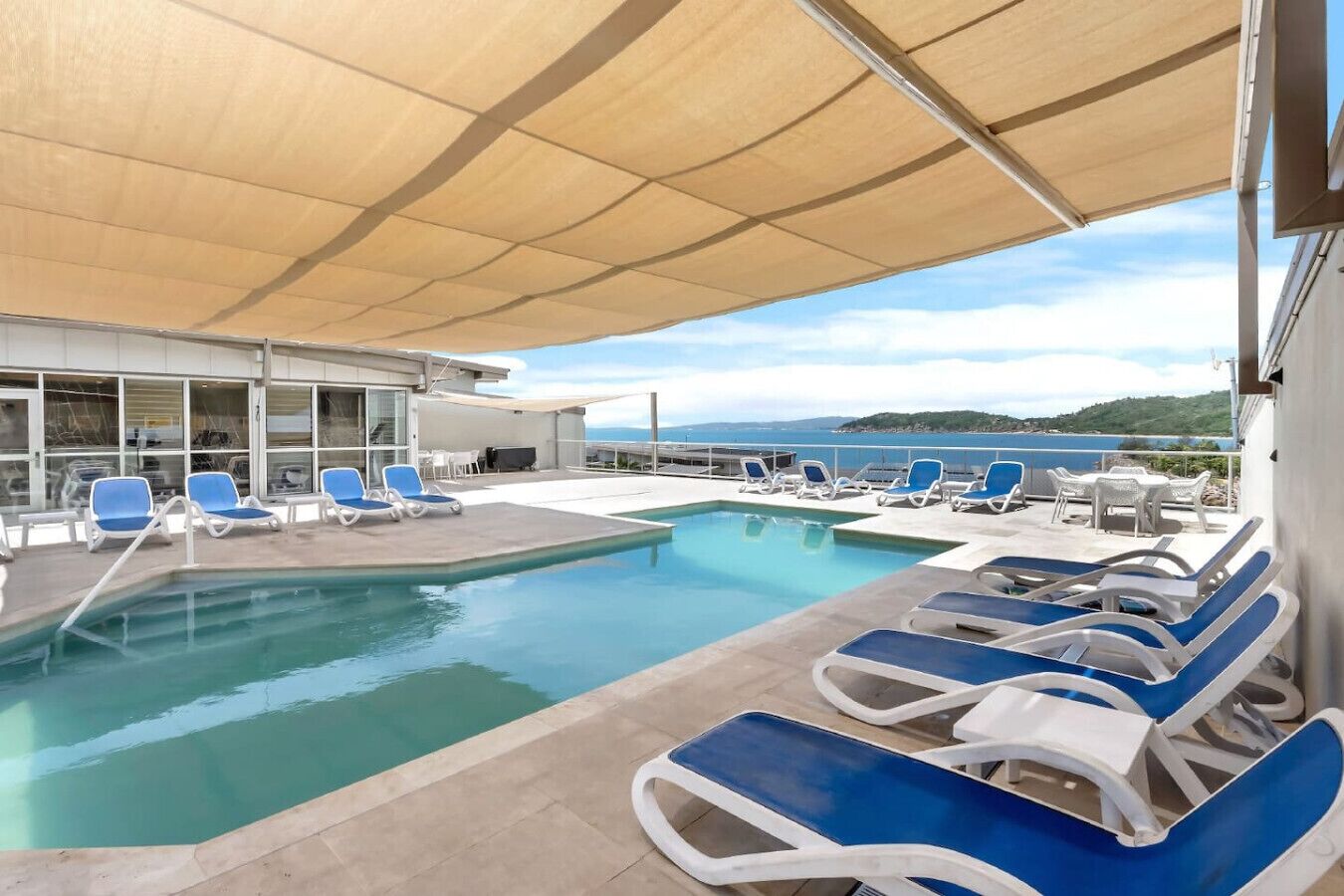 Ett poolområde med blå och vita solstolar, en pool och utsikt över havet.
