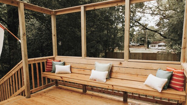 A wooden deck with a bench and cushions, surrounded by trees. - Stay & Play at the Charming Woodlawn Cottage (Hot Springs)