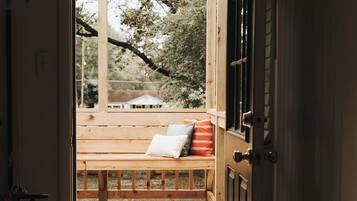 An open door leading to a wooden deck with a bench and cushions.