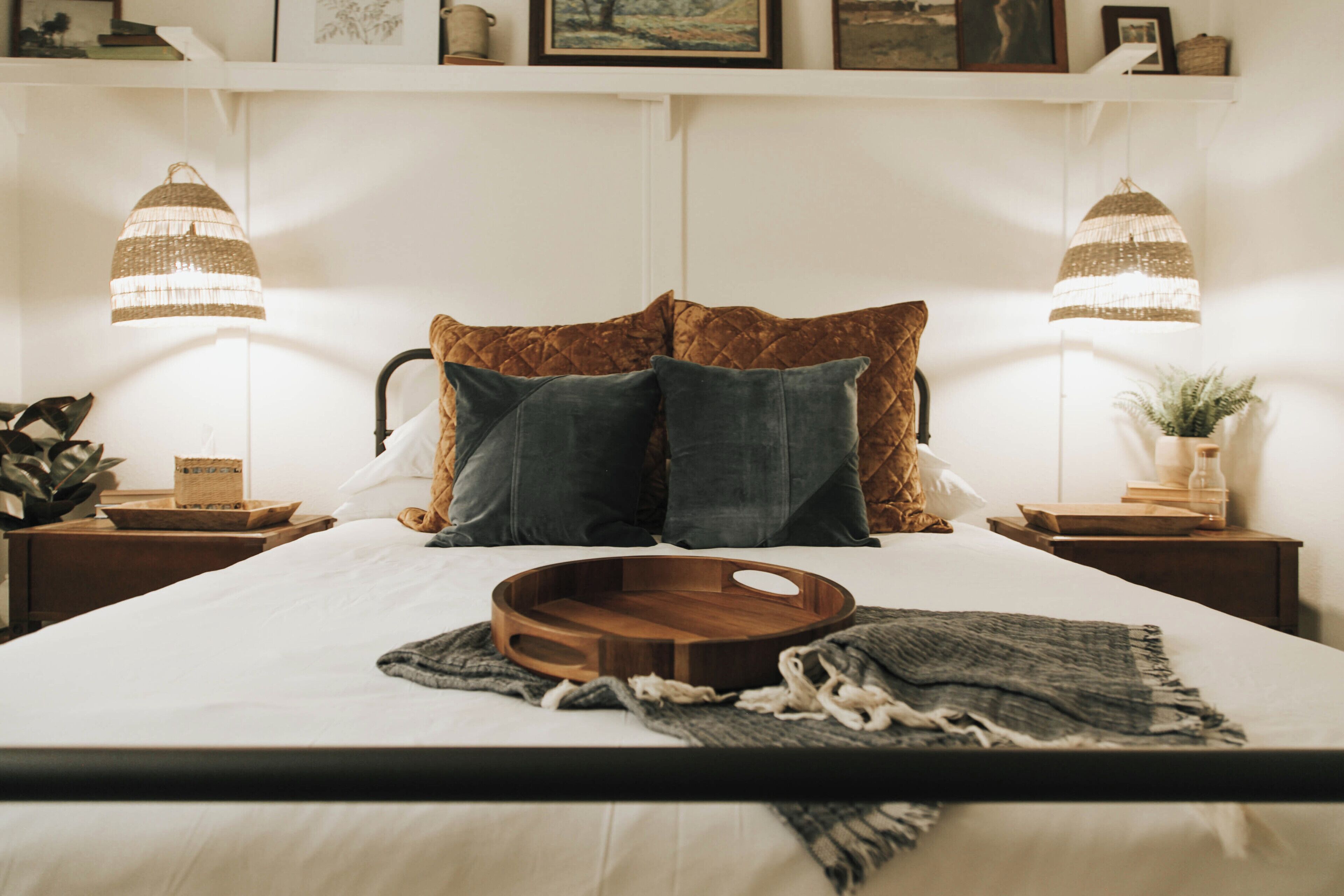A neatly made bed with a wooden tray and a blanket, flanked by two nightstands with lamps and a potted plant.