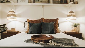 A neatly made bed with a wooden tray and a blanket, flanked by two nightstands with lamps and a potted plant. - Stay & Play at the Charming Woodlawn Cottage (Hot Springs)