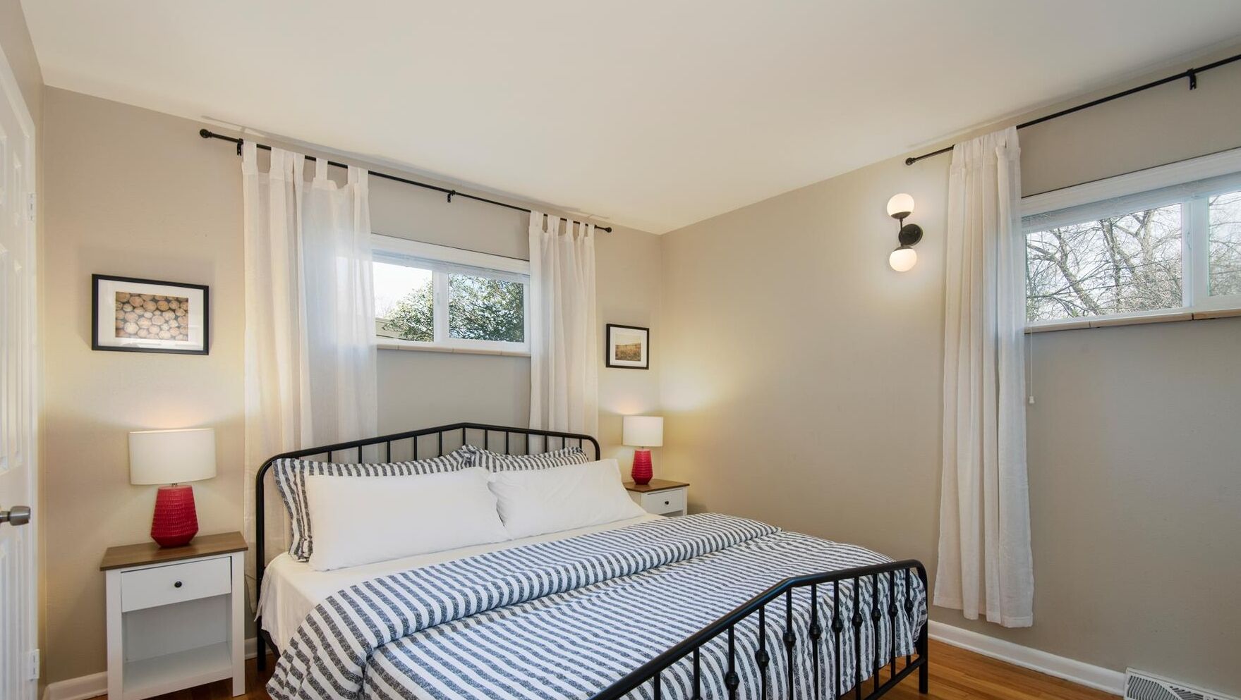 A bedroom with a bed, two bedside tables, a window with curtains, and wall-mounted light fixtures.