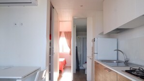 A compact kitchen with a sink, stove, and cabinets. A door leads to a bathroom with a toilet and shower. - Camping Village Torrenova (Ciro Marina)