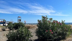 Ett område vid kusten med klar himmel, en strand och en byggnad med ett rött tak och ett torn.