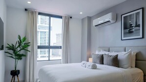 A modern hotel room with a large bed, a potted plant, an air conditioning unit, and a framed artwork on the wall.