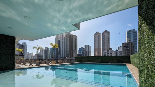 A rooftop pool with a city skyline view, surrounded by greenery and modern lounge chairs.