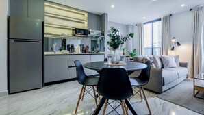 A modern kitchen with a built-in microwave and stove, a dining area with a round table and chairs, and a living area with a sofa and a large window.