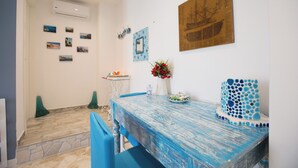 A dining area with a blue table, chairs, a vase with red flowers, and wall decorations including framed pictures and a ship painting.